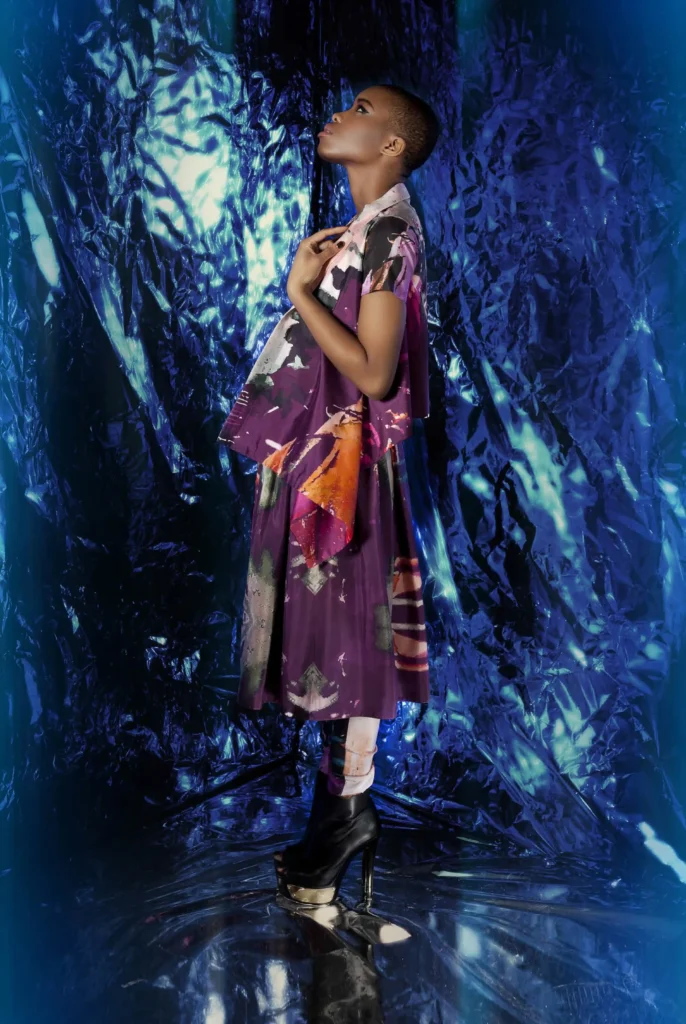 A rectangular street print draped jacket paired with a coordinated top, skirt, and ruched leggings, inspired by urban cityscapes and futuristic motion.